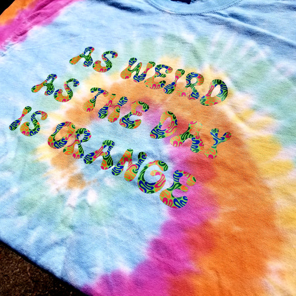 Pastel tie-dyed t-shirt printed in multicolor lettering that says as weird as the day is orange.