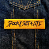 Orange patch with the words spooky shit for life embroidered in black thread.