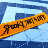 Orange patch with the words spooky shit for life embroidered in black thread.