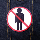 Round red and black on white embroidered patch of a no people allowed sign; a neutral figure crossed out with red.