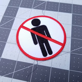 Round red and black on white embroidered patch of a no people allowed sign; a neutral figure crossed out with red.