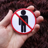 Round red and black on white embroidered patch of a no people allowed sign; a neutral figure crossed out with red. Shown in the palm of a hand for size reference.