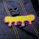 Neon green and purple on bright orange embroidered patch with the word, slimebag, and a oozing shaped border design.