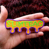 Neon green and purple on bright orange embroidered patch with the word, slimebag, and a oozing shaped border design.