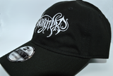 Left side view of a black baseball hat with a heavy metal style logo for the classical music composer Wagner embroidered on the front in white thread.