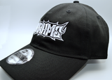 Left side view of a black baseball hat with a heavy metal style logo for the classical music composer Brahms embroidered on the front in white thread.