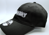 Left side view of a black baseball hat with a heavy metal style logo for the classical music composer Tchaikovsky embroidered on the front in white thread.