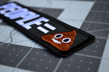 Close up detail of a rectangular black embroidered patch with that says people equals in white lettering followed by the poop emoji.