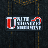Rectangular black embroidered patch with the words unite, unionize, undermine written in a stencil font, featuring a red sickle. Shown on a denim jacket.