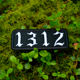A white on black rectangular embroidered patches with the number 1312.