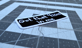 Close up detail of a rectangular black patch with a white border and the words, got that tism in me, embroidered in white thread.