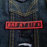Bad At Life embroidered patch in red on black.