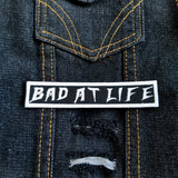 Bad At Life embroidered patch in white on black.