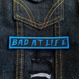 Bad At Life embroidered patch in blue on black.