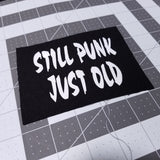 White on black screen printed canvas patch that says still punk, just old.