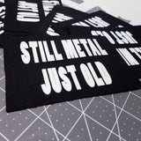 White on black screen printed canvas patch that says still metal, just old.