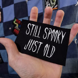 White on black screen printed canvas patch that says still spooky, just old. Shown in the palm of a hand for size reference.