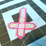 Inverted cross embroidered patch with hot pink and multicolor thread.