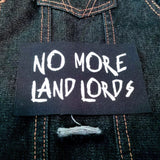 A white on black screen printed canvas patch that says no more landlords in graffiti lettering.