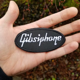 White on black Gibsiphone embroidered patch, a parody mashup of Gibson and Epiphone guitars, shown in a hand for size reference.