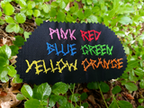 Black fabric swatch showing different thread colors stitched onto it as a color chart.