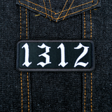 A white on black rectangular embroidered patches with the number 1312. Shown on a denim jacket.
