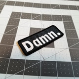 White on black embroidered patch with the word damn.