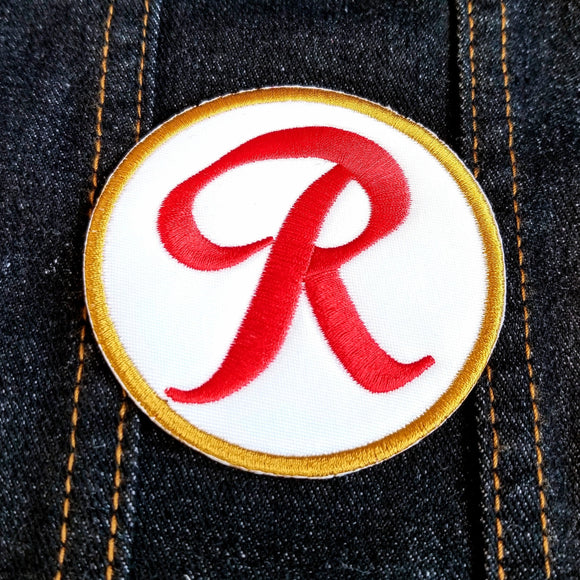 Round-shaped red, white, and gold Rainier Beer logo embroidered patch.