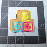 An embroidered patch of baby blocks with the numbers 6,6, and 6.