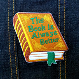 Embroidered book that says, the book is always better, on the cover.