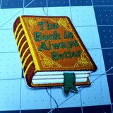 Embroidered book that says, the book is always better, on the cover.