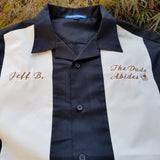 Black and stone colored bowling shirt inspired by The Big Lebowski, with the quote the dude abides embroidered on the left chest with a white russian cocktail and a custom name personalization embroidered on the right chest.