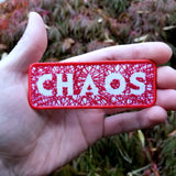 Red on white embroidered patch with hundreds of  random lines of thread spelling the word chaos. Shown in the palm of a hand for size reference.