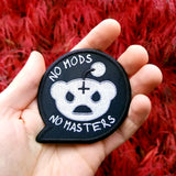 White on black embroidered patch in the shape of a speech bubble with a parody of the Reddit logo and the phrase, no mods no masters. Shown in the palm of a hand for size reference.