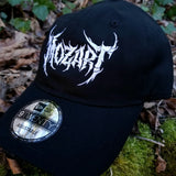 Black baseball cap with a heavy metal style logo for the classical music composer Mozart embroidered on the front in white thread.