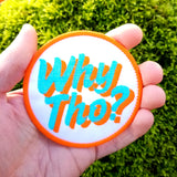 Circular embroidered patch with glittery blue and flat orange lettering saying why though on white fabric. Shown in the palm of a hand for size reference.