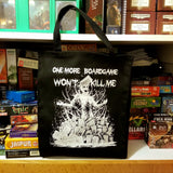 A black canvas tote bag with a white screen printed graphic of a zombie in a pile of boardgames and a caption saying one more boardgame won't kill me.