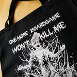 Close up detail of a black canvas tote bag with a white screen printed graphic of a zombie in a pile of boardgames and a caption saying one more boardgame won't kill me.