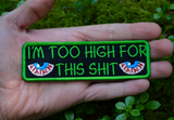 Rectangular green-bordered embroidered patch with a pair of bloodshot eyes and the text, I'm too high for this shit in green thread. Shown in the palm of a hand for size reference.