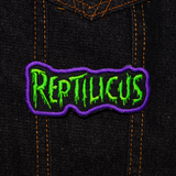 Embroidered patch with 'REPTILICUS' text in green on a black background with purple border. Shown on a denim jacket.