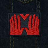 Rectangular black embroidered patch of the red hands of Manos, the Hands of Fate. Shown on a denim jacket.