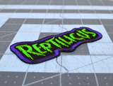 Embroidered patch with 'REPTILICUS' text in green on a black background with purple border.
