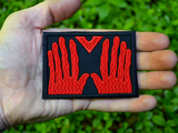 Rectangular black embroidered patch of the red hands of Manos, the Hands of Fate. Shown in the palm of a hand for size reference.