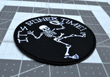 Close up detail of a round black embroidered patch with a dancing skeleton and the words it's boner time in white thread.