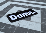 Close up detail of a rectangular black patch with white embroidery spelling the word damn with a period at the end.