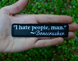 Rectangular black embroidered patch with a quote by Bonecrusher in white thread that says I hate people, man. Shown in the palm of a hand.