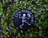 Round black embroidered patch with a dancing skeleton and the words it's boner time in white thread.