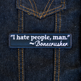 Rectangular black embroidered patch with a quote by Bonecrusher in white thread that says I hate people, man. Shown on a denim jacket.
