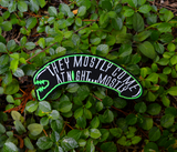 A black and green embroidered patch shaped like an alien head with the words, they mostly come at night, in grey thread.