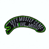 A black and green embroidered patch shaped like an alien head with the words, they mostly come at night, in grey thread.